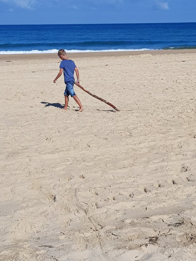 Kind loopt met een stok over het strand, peinzend bij de zee
