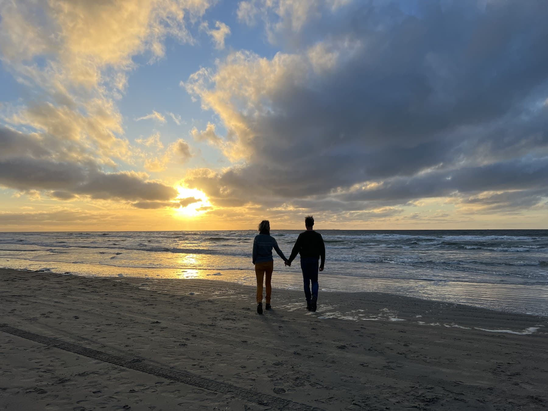 Twee mensen lopen hand in hand op het strand richting de zonsondergang